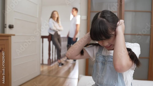 Stressed and unhappy young girl huddle in corner, cover her ears blocking sound of her parent arguing in background. Domestic violence at home and traumatic childhood develop to depression. Fastidious photo