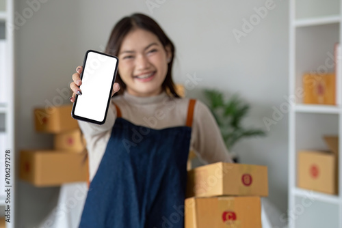 Beautiful smiling Asian woman holding a cardboard box and hands showing a smartphone mockup of a blank screen. Advertise your screen Online delivery concept