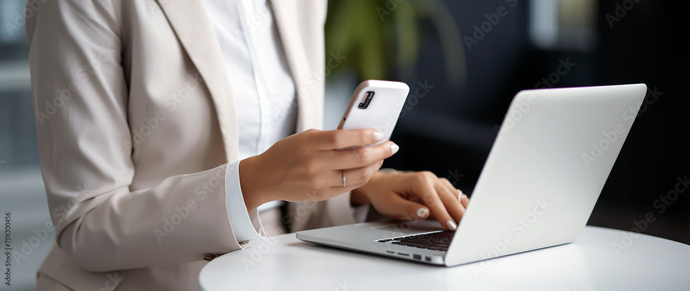 Business woman in grey suit using mobile phone while working on a laptop computer. Business woman in grey suit using mobile phone while working on a laptop computer.