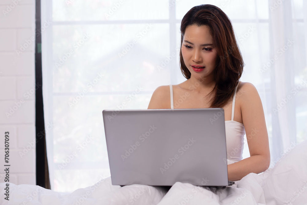 Happy beautiful asian woman working on a laptop sitting on the bed in the house. Happy beautiful asian woman working on a laptop sitting on the bed in the house.
