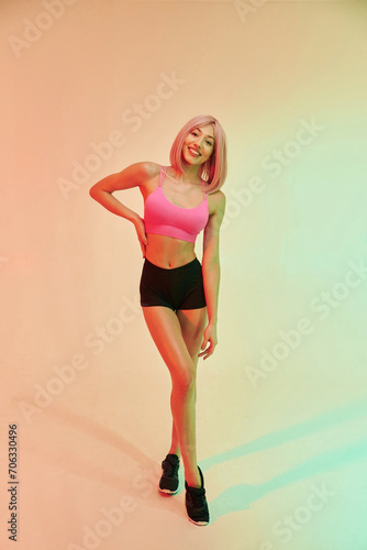 Standing and posing. Sportive woman with pink wig is against background