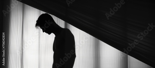 Silhouetted male body behind a white curtain in artistic photo.