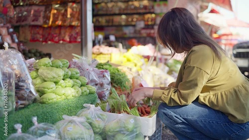 Young asian woman tourist choosing baby carrot at the local market. Healthy woman choosing fresh vegetables in the market. Vegetables and fruits concept photo