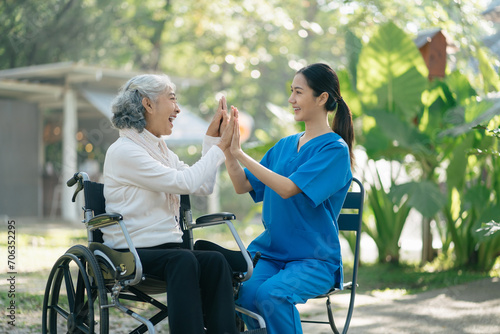 Smiling physiotherapist taking care of the happy senior patient in wheelchair, outdoor.