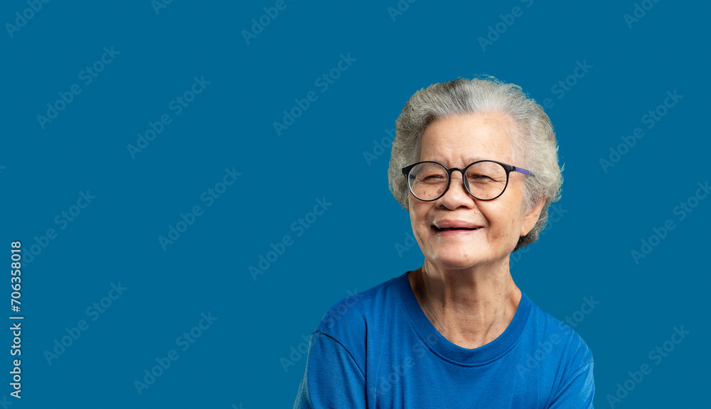 Portrait of an elderly Asian woman looking at the camera with a smile while standing on a blue background. Portrait of an elderly Asian woman looking at the camera with a smile while standing on a blue background.