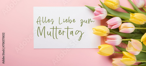 Alles Liebe zum Muttertag Feiertag Grußkarte - Weisses Papier, Rahmen mit deutschem Text und Tulpen auf pinkem Tisch Hintergrund, Draufsicht photo