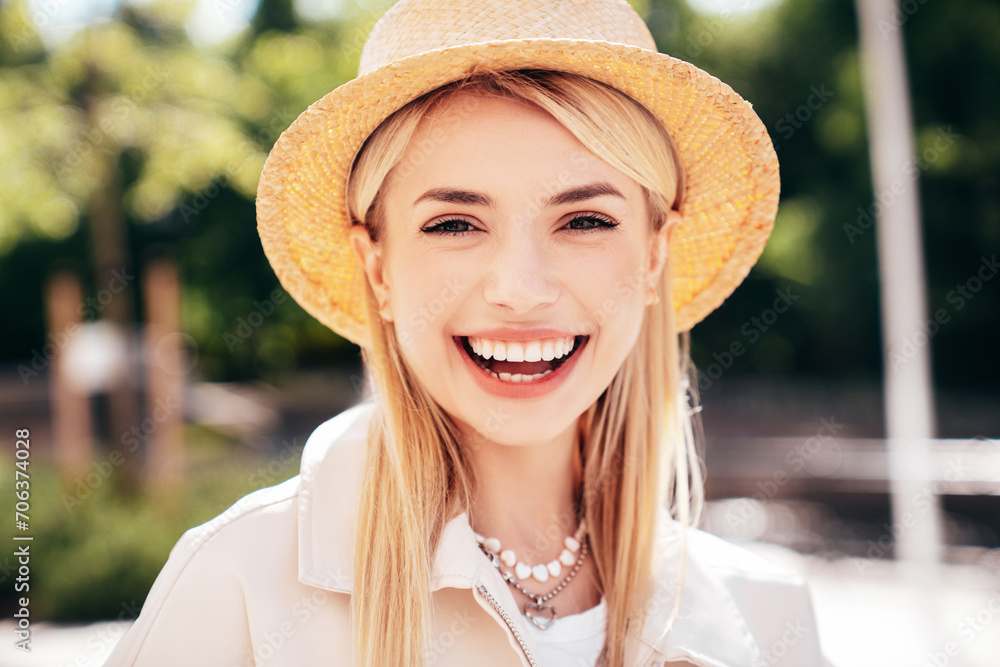 Young beautiful smiling blond woman in trendy summer clothes. Carefree female posing on the street background at sunny day. Positive model outdoors at sunset. Cheerful and happy in hat. Natural makeup