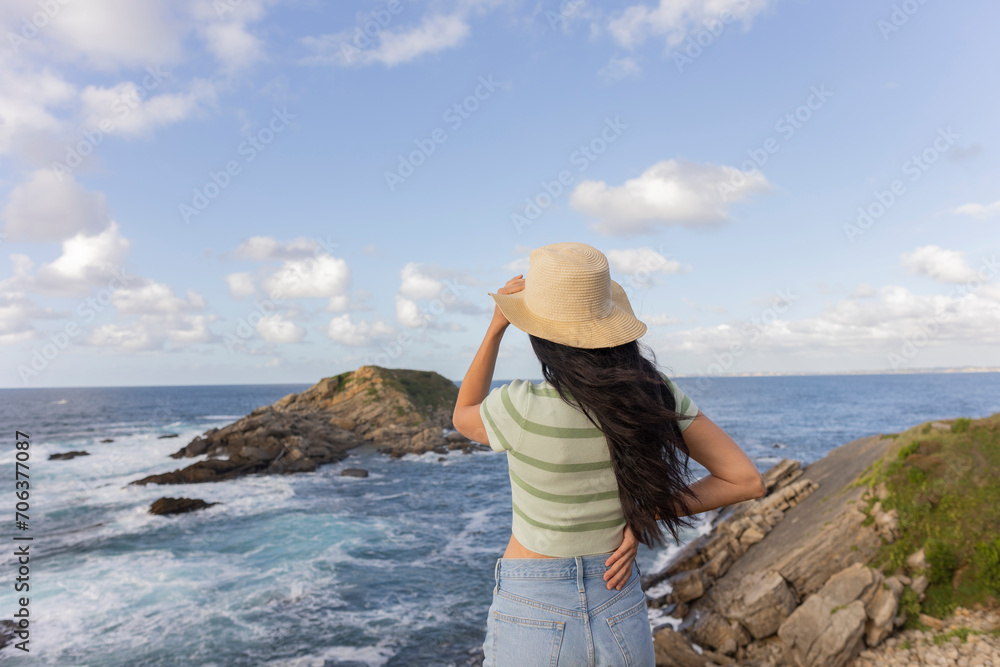 woman from behind holding her hat in the breeze with the maritime background