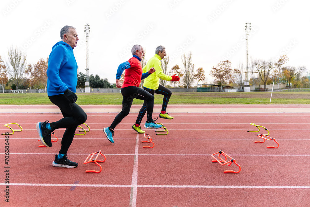 Fototapeta premium A trio of elderly men engaging in agility training with colorful hurdles on an athletic track