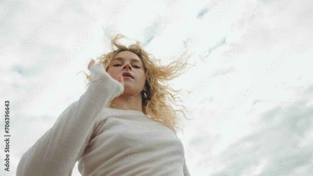 Young blonde woman performing contemporary dance, gazing at the camera against a backdrop of dramatic clouds Young blonde woman performing contemporary dance, gazing at the camera against a backdrop of dramatic clouds