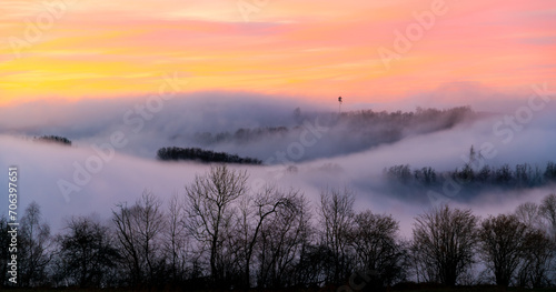 Panoramic view of foggy winter scenery in Sauerland Germany. Fluffy low mist clouds in the land of 1000 hills and valleys. Evening twilight after sunset with colorful sky gradient above the horizon.