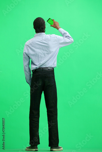 A man in a gray shirt, on a green background, in full height, waving a phone