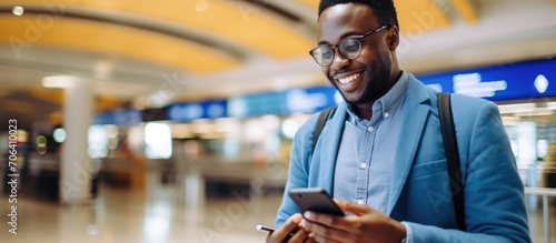 A black man with a smartphone app for booking, scheduling, and checking flight information at the airport for a business trip, feeling excited about his upcoming journey