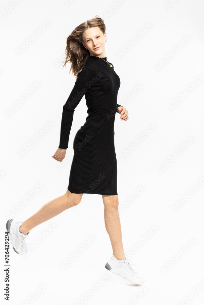 Portrait of young elegantly dressed young woman wearing black evening attire and white shoes jumping in elegant pose. Studio shot Portrait of young elegantly dressed young woman wearing black evening attire and white shoes jumping in elegant pose. Studio shot