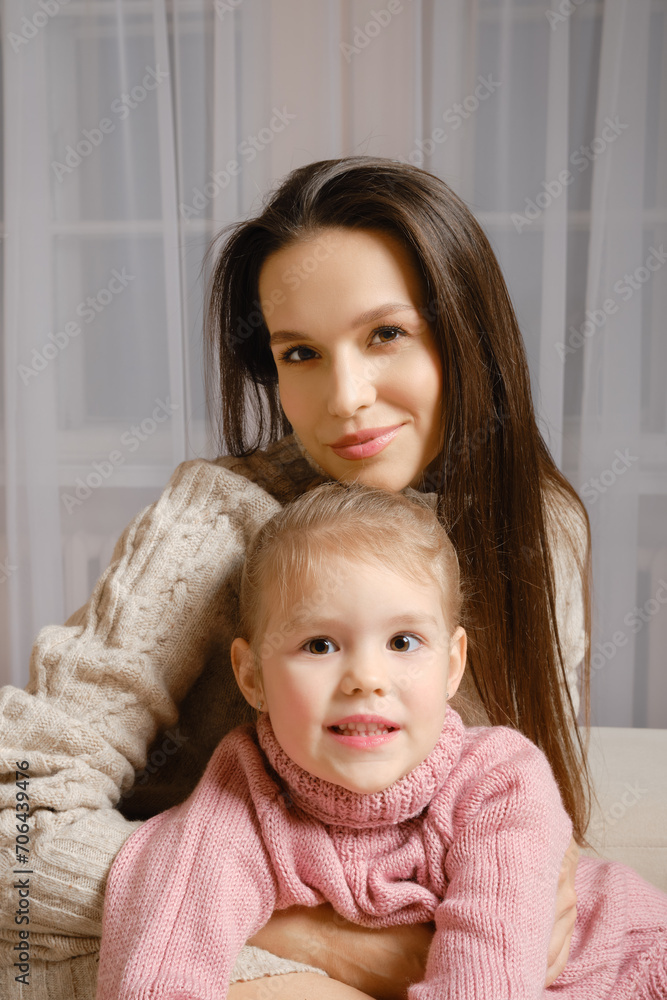 A mother and daughter sit together in a cozy home setting wearing knitted sweaters A mother and daughter sit together in a cozy home setting wearing knitted sweaters