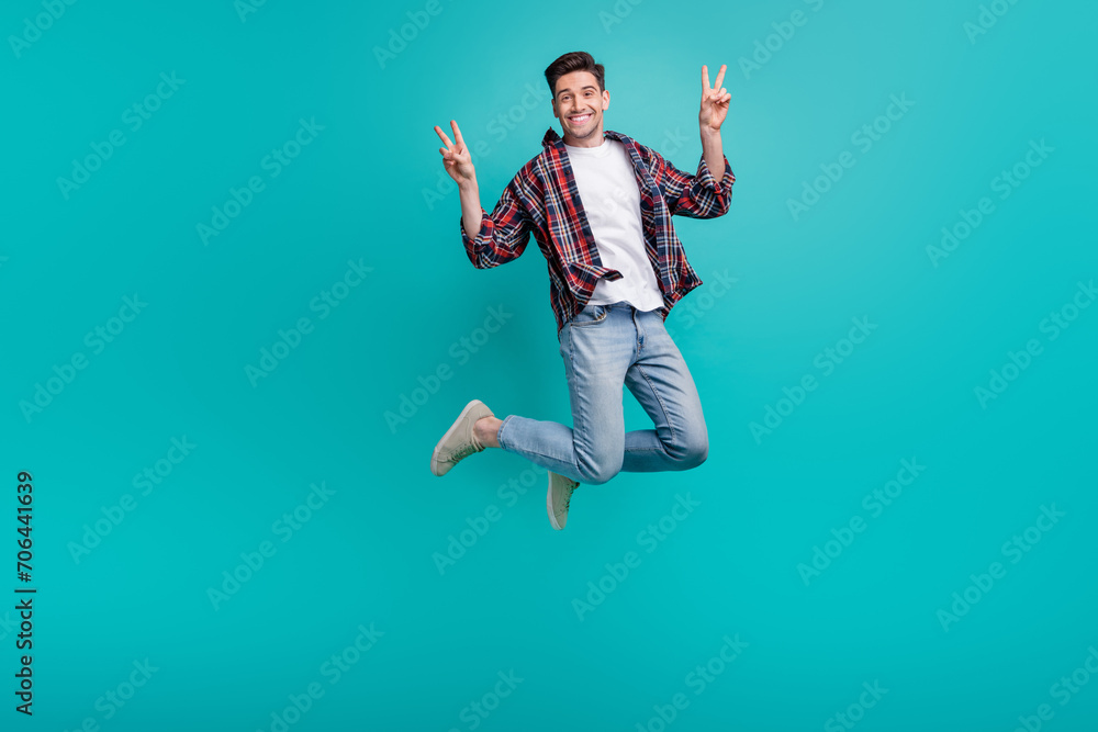 Full length photo of funny cheerful man dressed plaid shirt jumping high showing two v-signs isolated turquoise color background