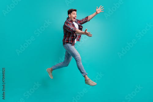 Full length photo of funky good mood man dressed plaid shirt jumping high catching arms empty space isolated turquoise color background