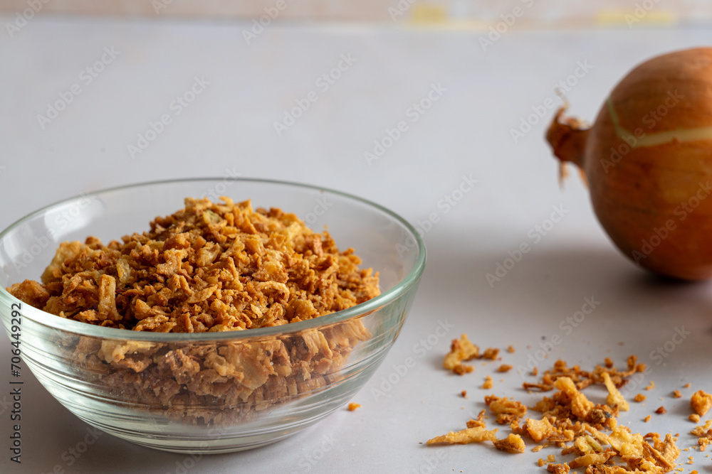 Golden crispy fried onion flakes in a glass dish on a white background. Golden crispy fried onion flakes in a glass dish on a white background.