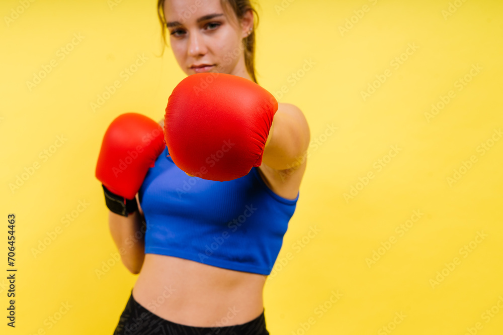 Woman boxer in gloves training on grey and yellow background studio