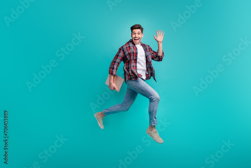 Full length photo of excited friendly man dressed plaid shirt jumping walking waving arm holding gadget isolated turquoise color background © deagreez