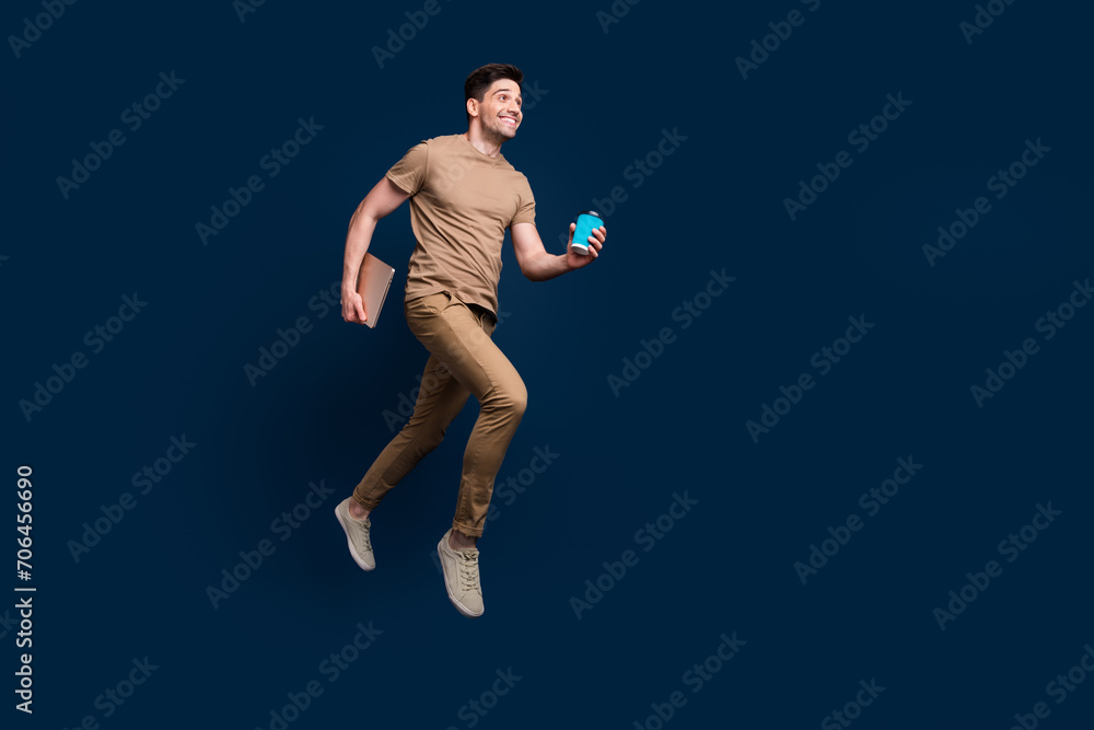 Full size photo of excited man dressed beige t-shirt running with laptop latte look empty space isolated on dark blue color background