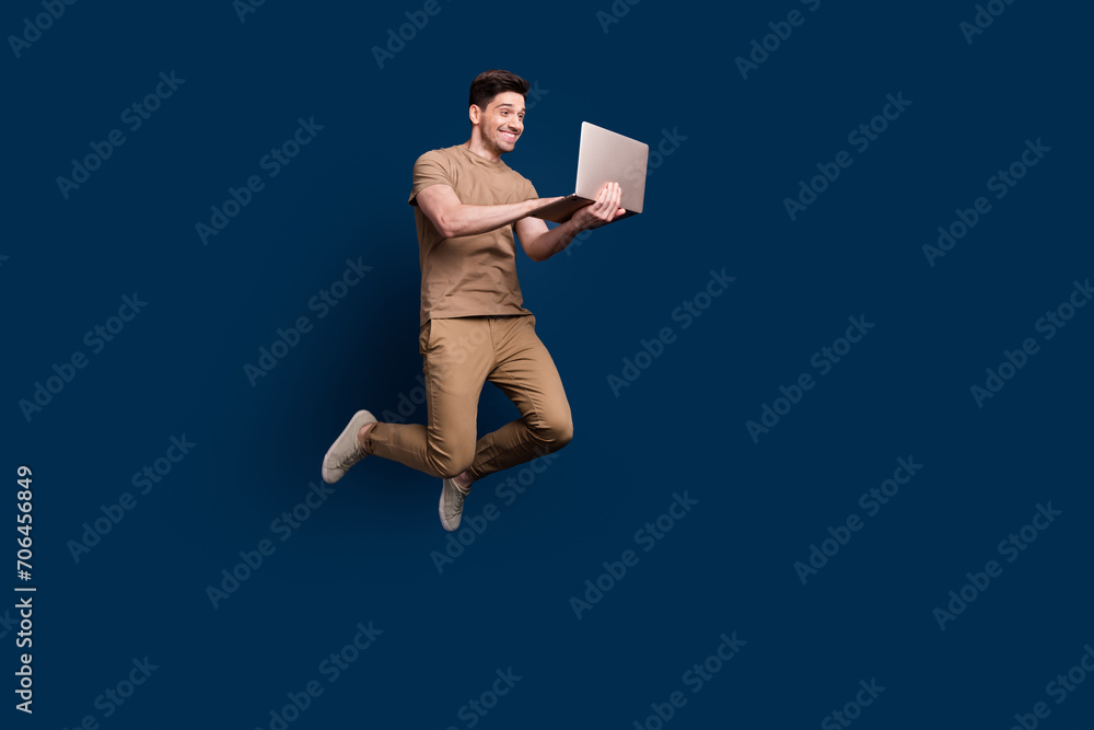 Full size photo of cheerful pleasant smart man wear beige outfit jumping chatting on laptop isolated on dark blue color background