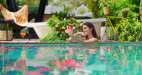 Wall Mural Indian Asian smiling young adult wet girl blue water pool edge take selfie record video use mobile look phone cam outdoor home