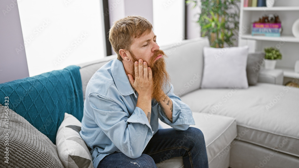 Depressed young redhead man, stressed and alone, sitting on the sofa at home, grappling with mental crisis and anxiety Depressed young redhead man, stressed and alone, sitting on the sofa at home, grappling with mental crisis and anxiety