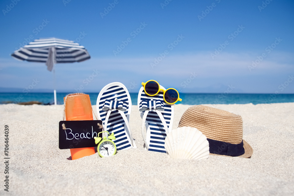 Obraz premium A Beach summer holiday banner background. Flip-flops and hat with a board and ball on the sand near the ocean. Summer accessories on the seashore. 