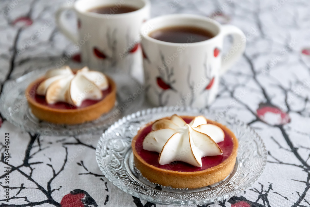 Tartlet cake with meringue and cups of tea on the table. Bullfinch pattern on tablecloths and cups. Photo