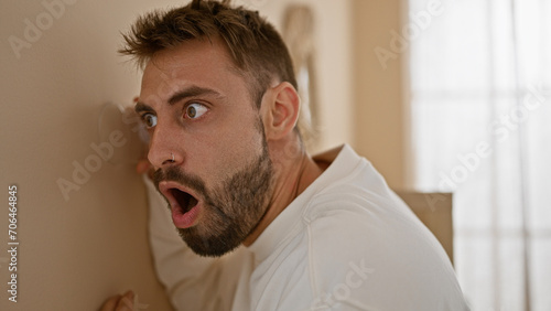 Bilde på lerret Curious young hispanic man surprised while eavesdropping through wall at home us