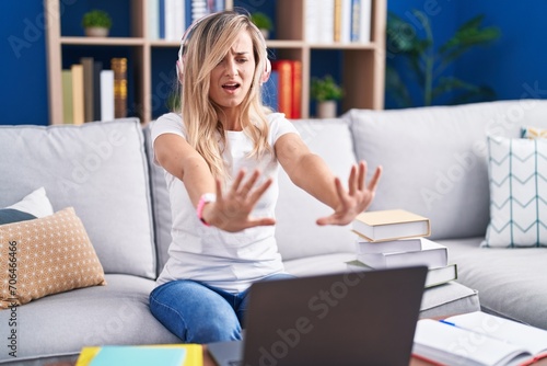 Young blonde woman studying using computer laptop at home doing stop gesture with hands palms, angry and frustration expression