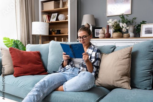 Young religious woman is sitting at home, happy because she found faith while reading books about religion. Believer female enjoying her time knowing about God.
