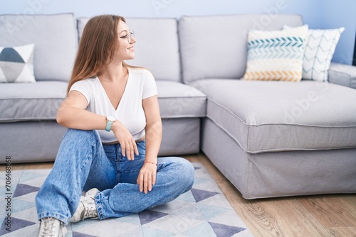 Young caucasian woman sitting on the floor at the living room looking to side, relax profile pose with natural face and confident smile.