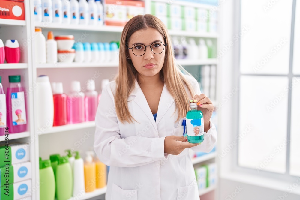 Young blonde woman working at pharmacy drugstore holding syrup skeptic and nervous, frowning upset because of problem. negative person.