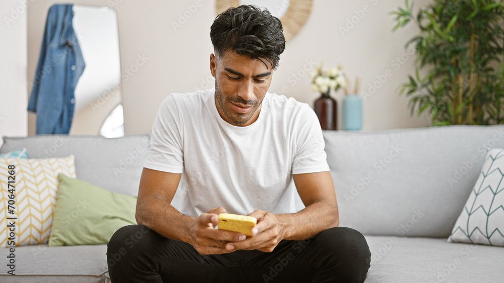 Handsome hispanic man using smartphone in a cozy living room Handsome hispanic man using smartphone in a cozy living room