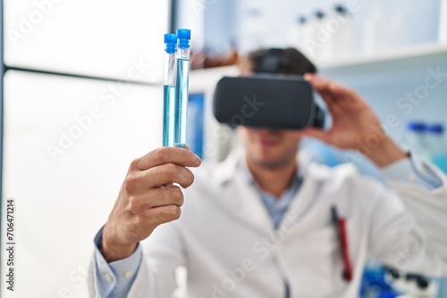 Young hispanic man scientist using virtual reality glasses holding test tubes at laboratory