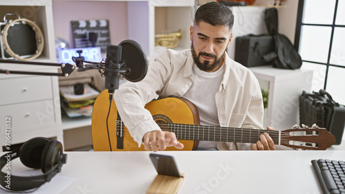 Handsome man recording acoustic guitar music in a modern indoor studio setup, showcasing creativity and performance.