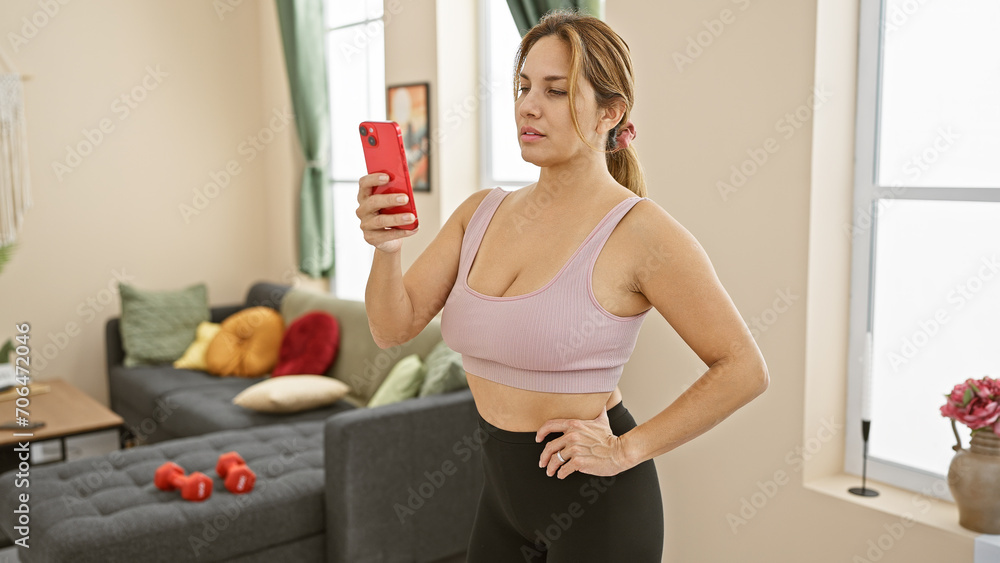 Hispanic woman taking selfie in her living room with smartphone, fitness attire, confident Hispanic woman taking selfie in her living room with smartphone, fitness attire, confident