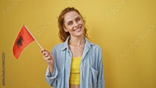 Bild auf Leinwand Smiling caucasian woman holding an albanian flag against a yellow backdrop, conveying national pride and joy