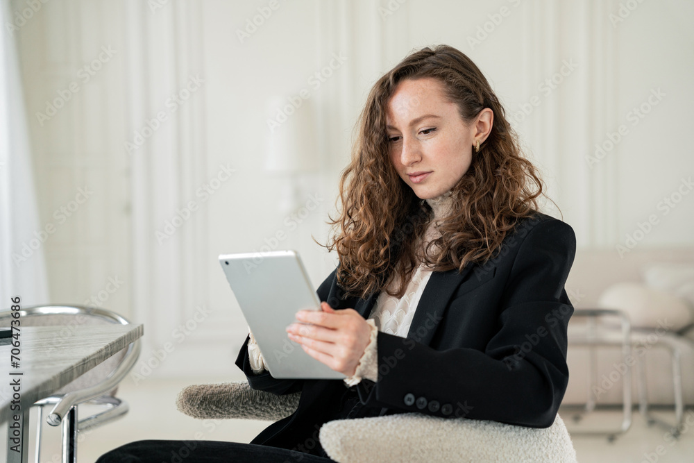 Professional woman intently using a tablet in a chic, modern lounge setting. Professional woman intently using a tablet in a chic, modern lounge setting.