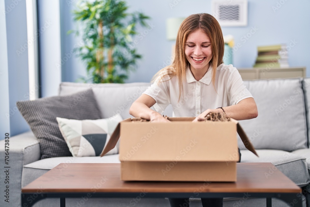 Young blonde woman unpacking cardboard box at home Young blonde woman unpacking cardboard box at home