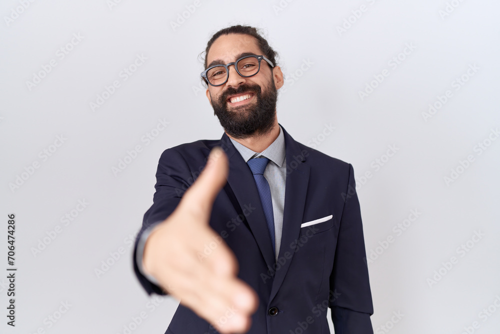 Hispanic man with beard wearing suit and tie smiling friendly offering handshake as greeting and welcoming. successful business. Hispanic man with beard wearing suit and tie smiling friendly offering handshake as greeting and welcoming. successful business.