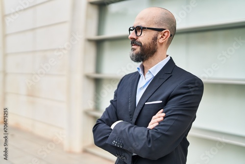 Young bald man business worker standing with arms crossed gesture at street