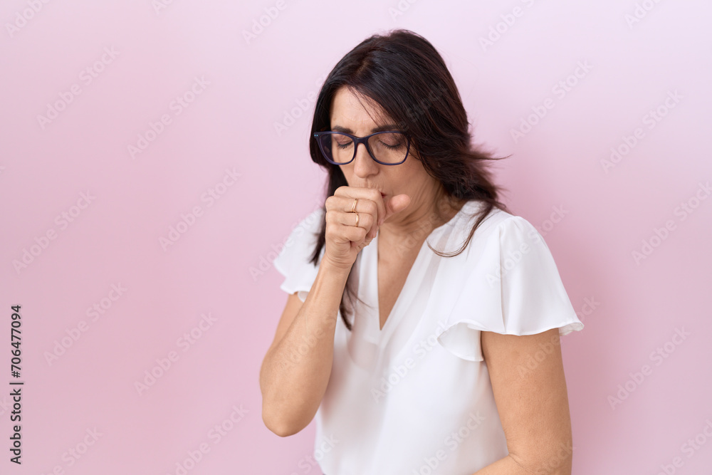Middle age hispanic woman wearing casual white t shirt and glasses feeling unwell and coughing as symptom for cold or bronchitis. health care concept. Middle age hispanic woman wearing casual white t shirt and glasses feeling unwell and coughing as symptom for cold or bronchitis. health care concept.