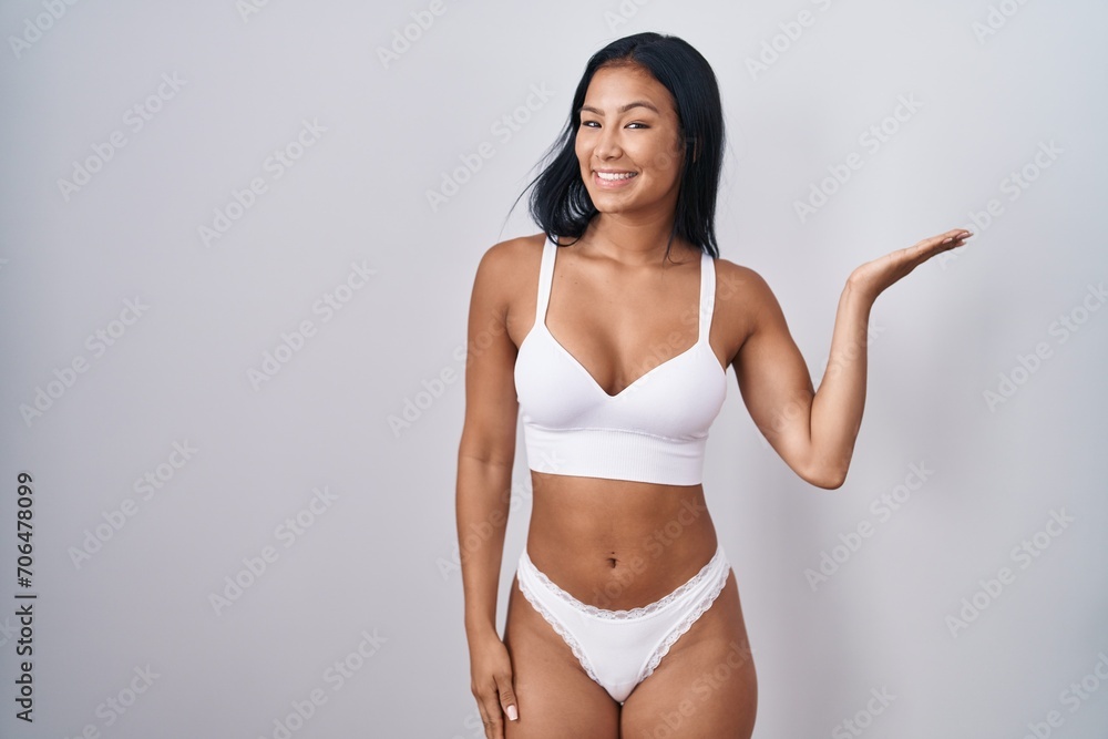 Hispanic woman wearing lingerie smiling cheerful presenting and pointing with palm of hand looking at the camera. Hispanic woman wearing lingerie smiling cheerful presenting and pointing with palm of hand looking at the camera.