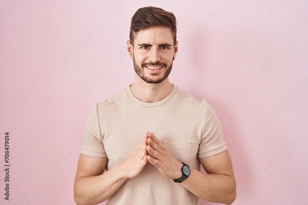 Hispanic man with beard standing over pink background hands together and fingers crossed smiling relaxed and cheerful. success and optimistic Hispanic man with beard standing over pink background hands together and fingers crossed smiling relaxed and cheerful. success and optimistic