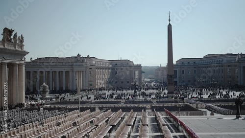 Rome, Italy - 25 May, 2023: Panoramic scene of St. Peter square in Rome with crowd of tourist people in large row waiting for entrance in basilica. Empty chairs for Eastern mass ceremony. photo