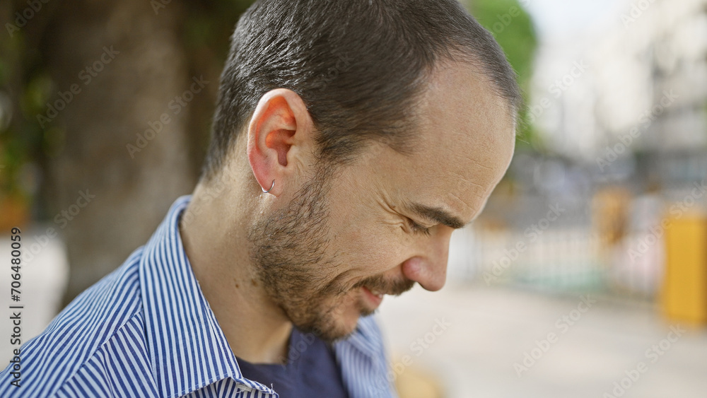 Hispanic man with beard, no hair, smiling in a casual setting, outdoors on an urban street. Hispanic man with beard, no hair, smiling in a casual setting, outdoors on an urban street.