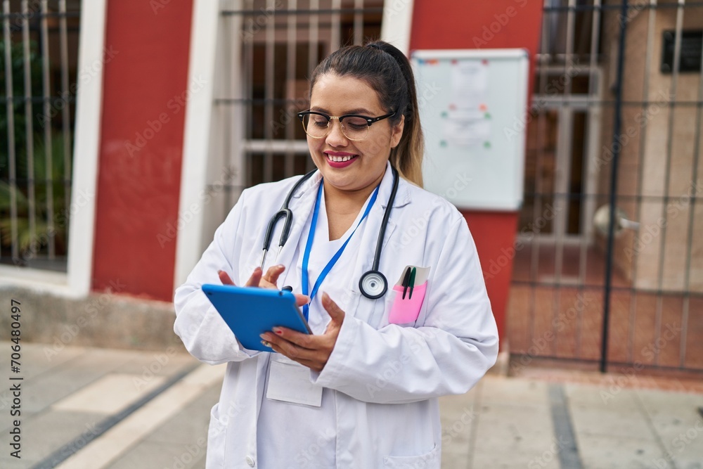 Young beautiful plus size woman doctor smiling confident using touchpad at hospital
